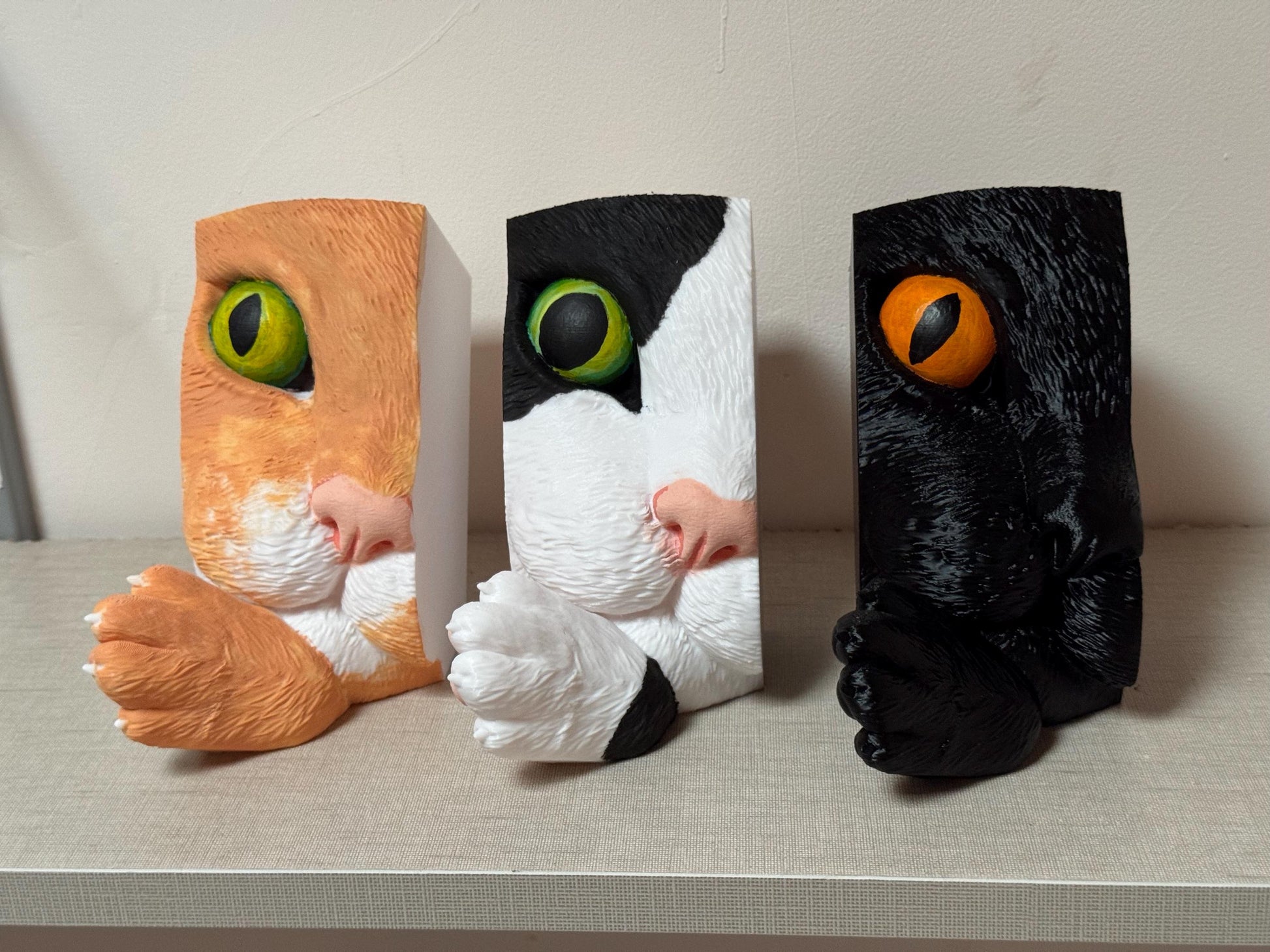 Three cat-shaped cushions with different color schemes on a neutral background