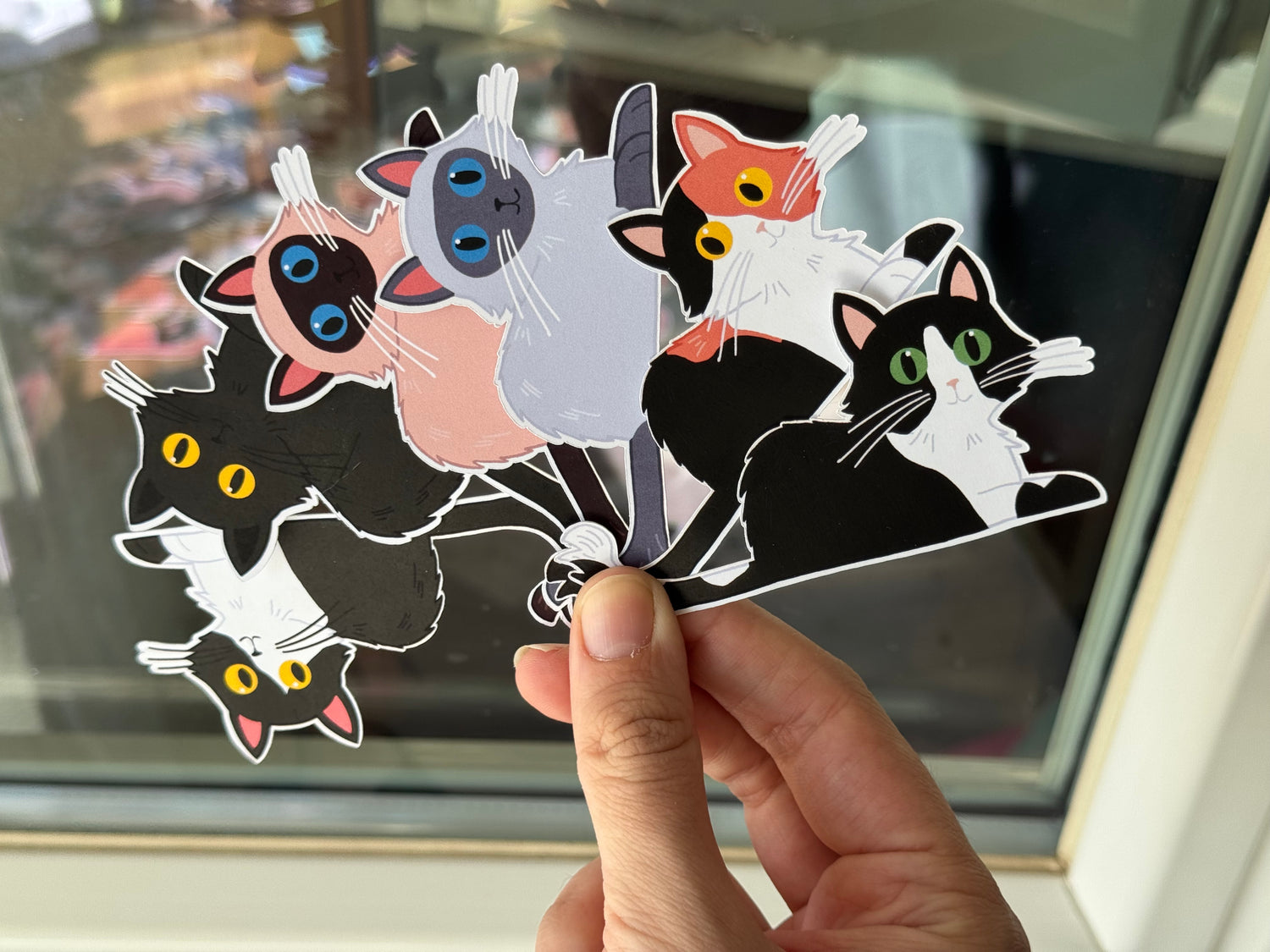 Hand holding a set of colorful long hair cat-shaped stickers 